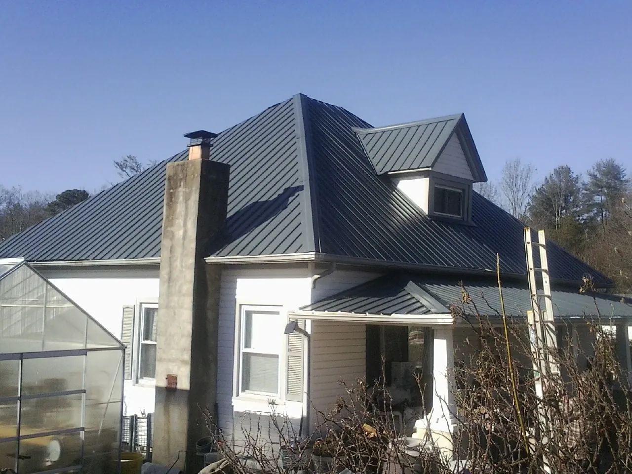 Dark blue standing seam metal roof on a white farmhouse with dormer — Slate & Tile Roof Repair by Roofing Brothers in Jelm