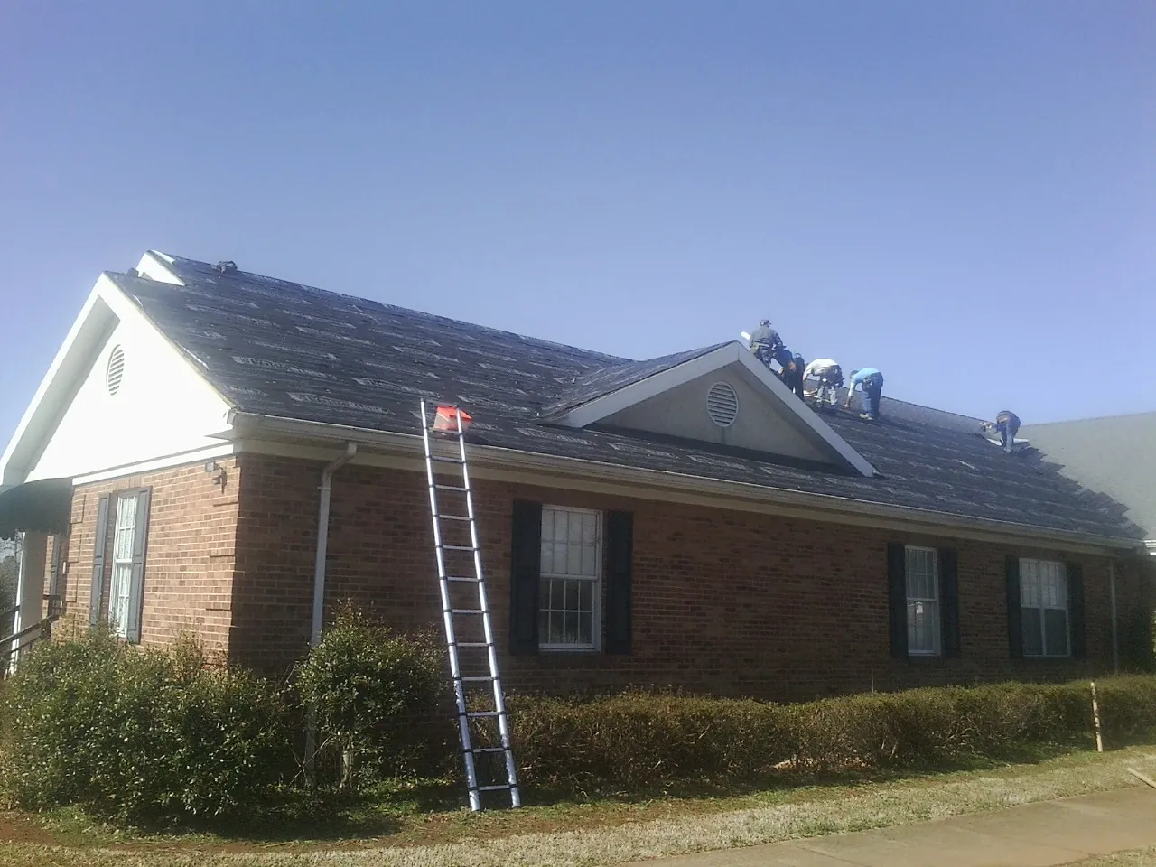 Crew tearing shingles off a brick ranch roof with a ladder set — Emergency Roof Repair work by our crew in Jelm