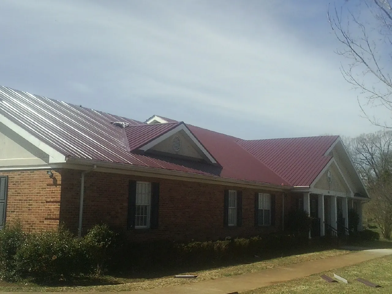 Red metal roof with gabled entries on a long brick building, from a Hail Damage Roof Repair job in Jelm