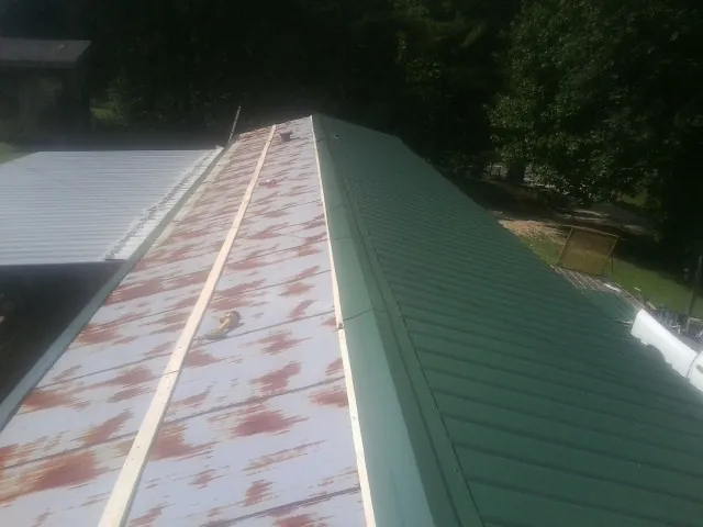 Old rusted panels beside newly installed green metal roofing — Wind Damage Roof Repair by Roofing Brothers in Jelm