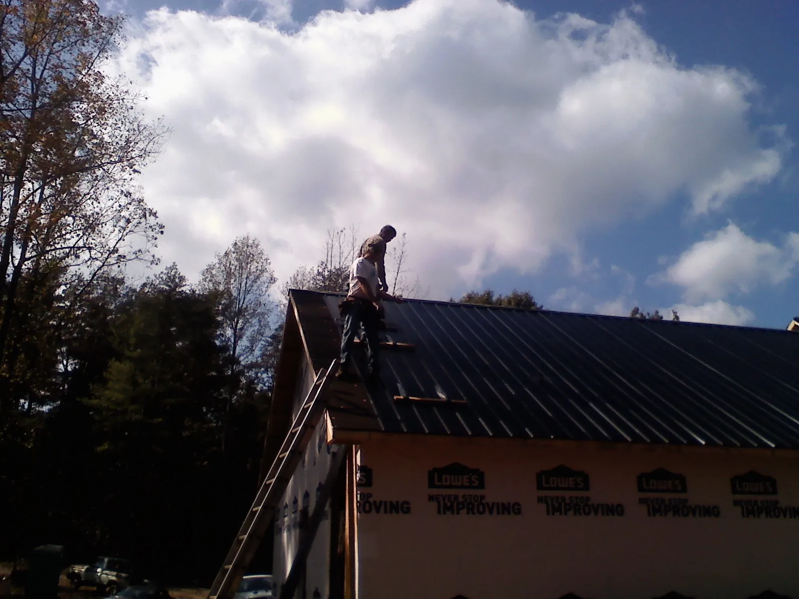 Roofer fastening dark metal panels high against a cloudy sky, from a Roof Inspection job in Jelm
