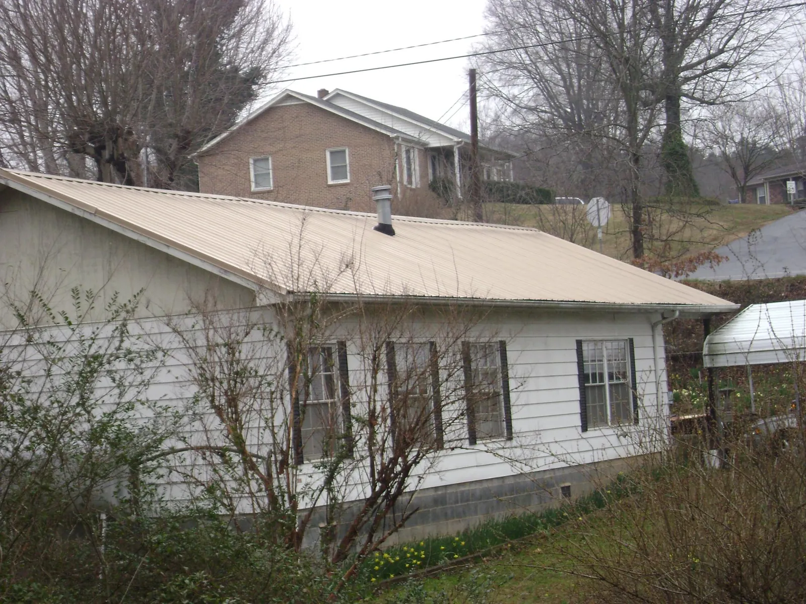 Tan metal roof on a white sided house set into a hillside — Commercial Roofing by Roofing Brothers in Jelm